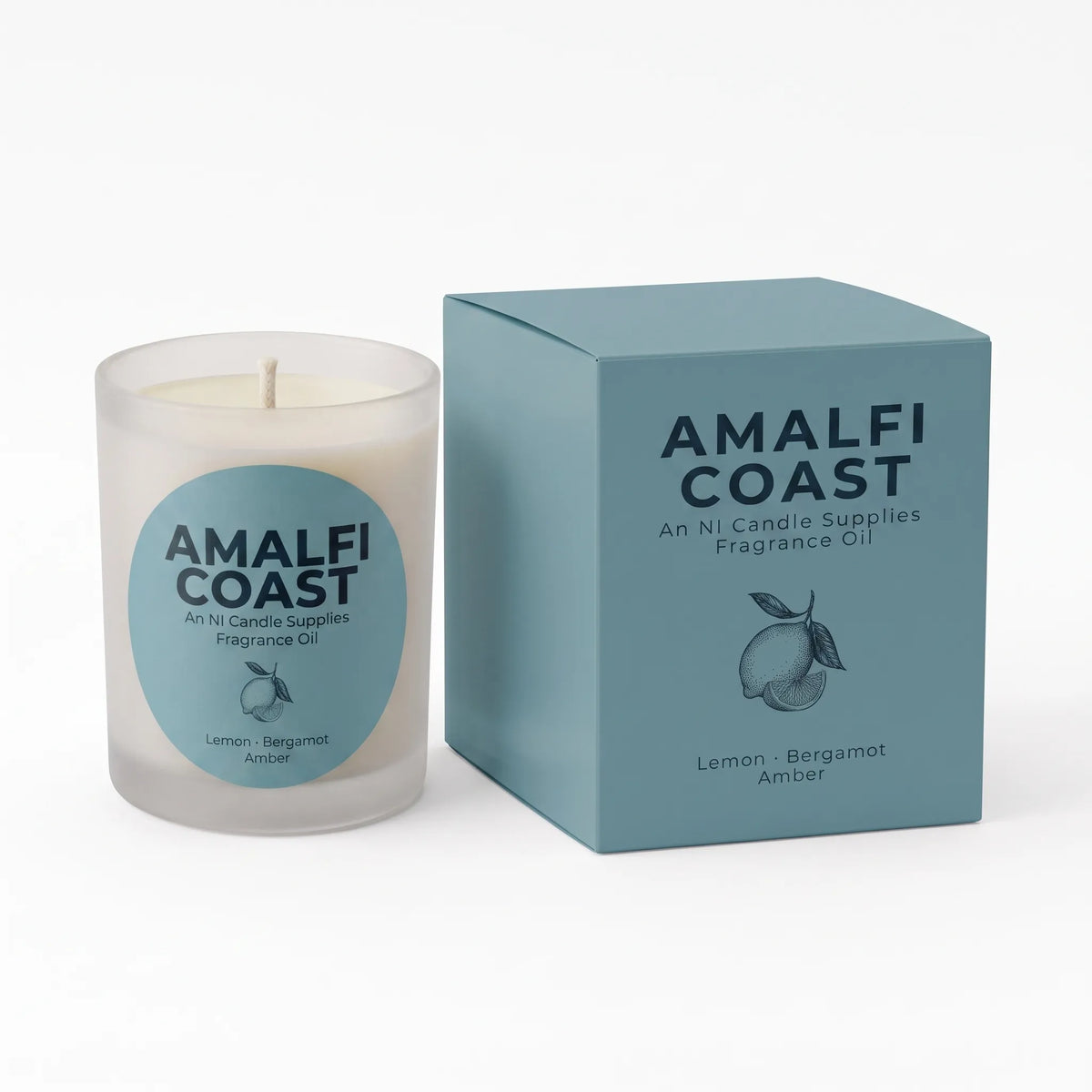 A frosted glass candle jar with a white wax and wick next to its matching dusty blue packaging box. Both pieces feature the brand name 'AMALFI COAST' and scent details for 'Lemon Bergamot Amber'.