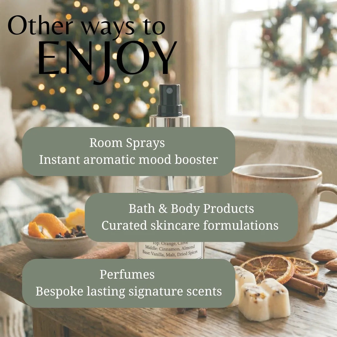 A perfume or room spray bottle is centered on a wooden table with overlaid marketing text reading 'Other ways to ENJOY' and three callouts about room sprays, bath & body products, and perfumes. The scene includes a mug, dried orange slices, cinnamon, marshmallows, and a softly blurred holiday window background.