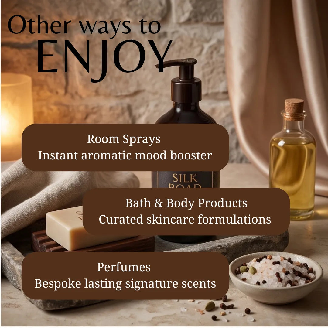 Promotional graphic for a fragrance and bath/body collection, featuring a dark amber pump bottle labeled SILK ROAD, a small glass oil bottle, a bar of soap, and a bowl of coarse salt on a stone tray with a lit candle. Text overlays read 'Other ways to ENJOY,' 'Room Sprays Instant aromatic mood booster,' 'Bath & Body Products Curated skincare formulations,' and 'Perfumes Bespoke lasting signature scents.