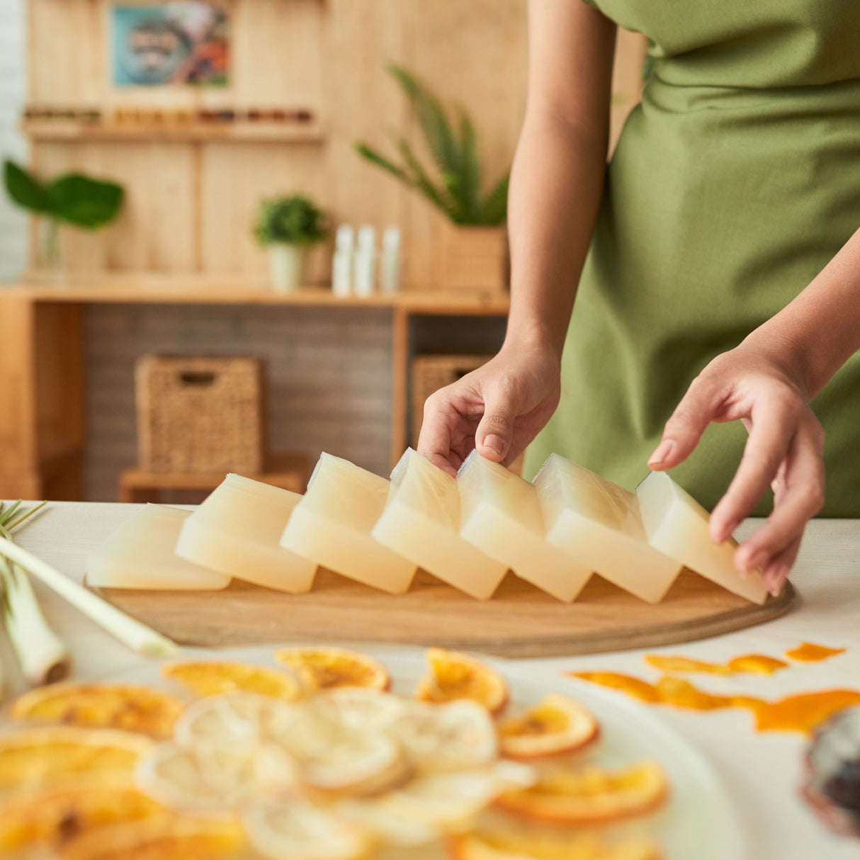 Person arranging slices of home made soap on a wooden board with a kitchen background
