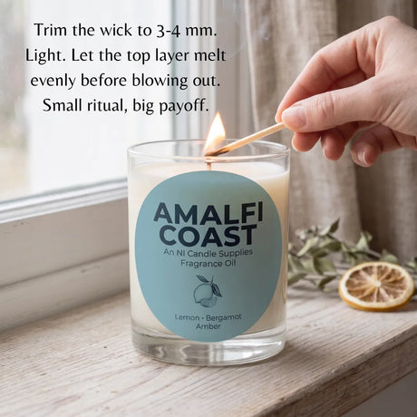 A clear glass jar candle labeled AMALFI COAST sits on a windowsill with a hand lighting it with a wooden match. Text on the image explains how to light the candle.