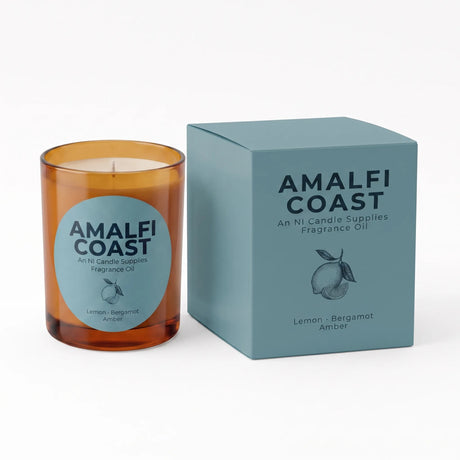 An amber glass candle jar with a light blue circular label next to its matching light blue box, both branded AMALFI COAST, on a clean white background.