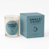 A candle in a clear glass jar with cream-colored wax and a round light blue label, shown next to its matching light blue box. The label and box read 'AMALFI COAST' and 'Lemon Bergamot Amber'.