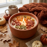 Candle with leaf decorations on a wooden table with pumpkins and a mug.