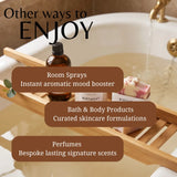 Promotional graphic for home fragrance and bath products, showing a wooden bath caddy over a bathtub with an amber spray bottle, a bar of soap, and overlaid text reading 'Other ways to ENJOY' plus categories for room sprays, bath & body products, and perfumes.