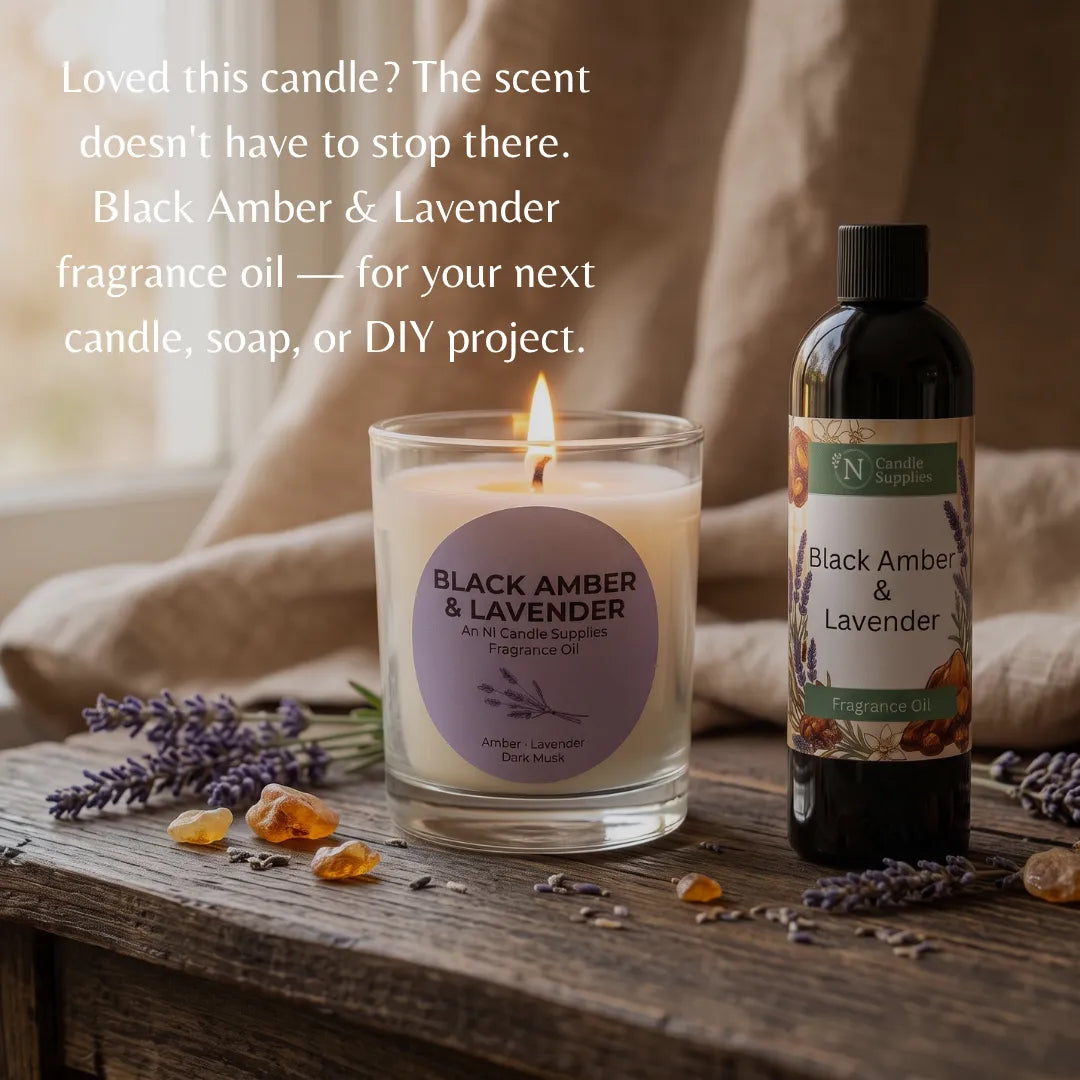 A lit candle in a clear glass jar and a bottle of Black Amber & Lavender fragrance oil are displayed on a rustic wooden surface with lavender sprigs, amber stones, and draped fabric in the background. White promotional text appears on the left side.