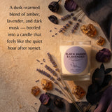 A glass jar candle labeled 'BLACK AMBER & LAVENDER' sits on a textured beige surface surrounded by dried lavender sprigs, amber crystals, and dark dried leaves. A descriptive text overlay appears on the left side.