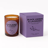 An amber glass scented candle with a lavender label sits next to its purple packaging box on a clean white background. The box is labeled 'BLACK AMBER & LAVENDER' by 'An NI Candle Supplies'.