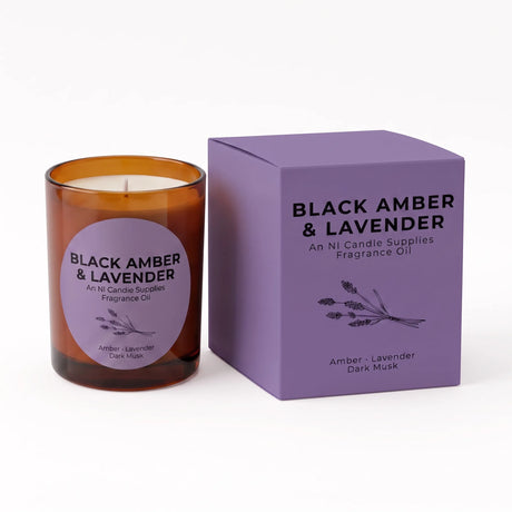 An amber glass scented candle with a lavender label sits next to its purple packaging box on a clean white background. The box is labeled 'BLACK AMBER & LAVENDER' by 'An NI Candle Supplies'.