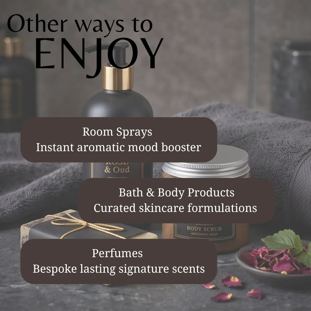 Promotional graphic for a fragrance and body product collection, featuring a dark bottle with a gold pump, a jar labeled BODY SCRUB, and gift packaging on a gray towel with rose petals. Large text reads 'Other ways to ENJOY' with callouts for room sprays, bath & body products, and perfumes.