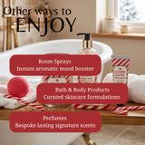 Promotional graphic for a bath and body product collection in a bathroom setting. The scene shows a pump bottle, a tube labeled 'CANDY CANE HAND CREAM,' a red bath bomb, rolled towels, and candy cane props on a wooden bench beside a bathtub.