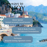 Scenic view of a coastal town with mountains in the background, featuring text about room sprays, bath & body products, and perfumes.