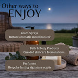 Promotional graphic with the headline 'Other ways to ENJOY' over a nighttime outdoor scene by the water, showing several product containers and bars arranged on a table with text callouts for room sprays, bath & body products, and perfumes.