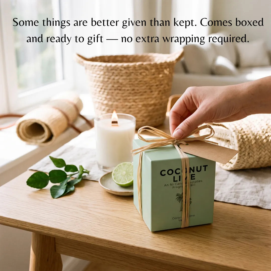 A hand holds the bow of a small mint green gift box labeled 'COCONUT LITE' on a wooden table, with a lit candle, lime, rolled fabric, and woven basket in a bright room. Text at the top reads, 'Some things are better given than kept.