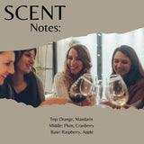 Scent Notes graphic showing a photo of four women smiling and holding wine glasses, with text listing fragrance notes: Orange, Mandarin; Plum, Cranberry; Raspberry, Apple.
