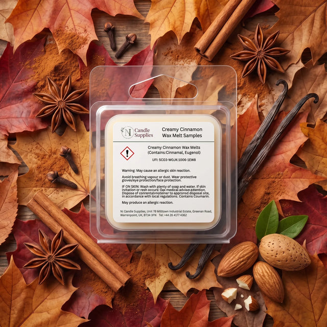 A clear plastic clamshell package labeled 'Creamy Cinnamon Wax Melt Samples' by Candle Supplies, placed on a styled flat lay of autumn leaves, cinnamon sticks, star anise, vanilla beans, and almonds. The product packaging is centered against a warm, textured background of brown and orange leaves.