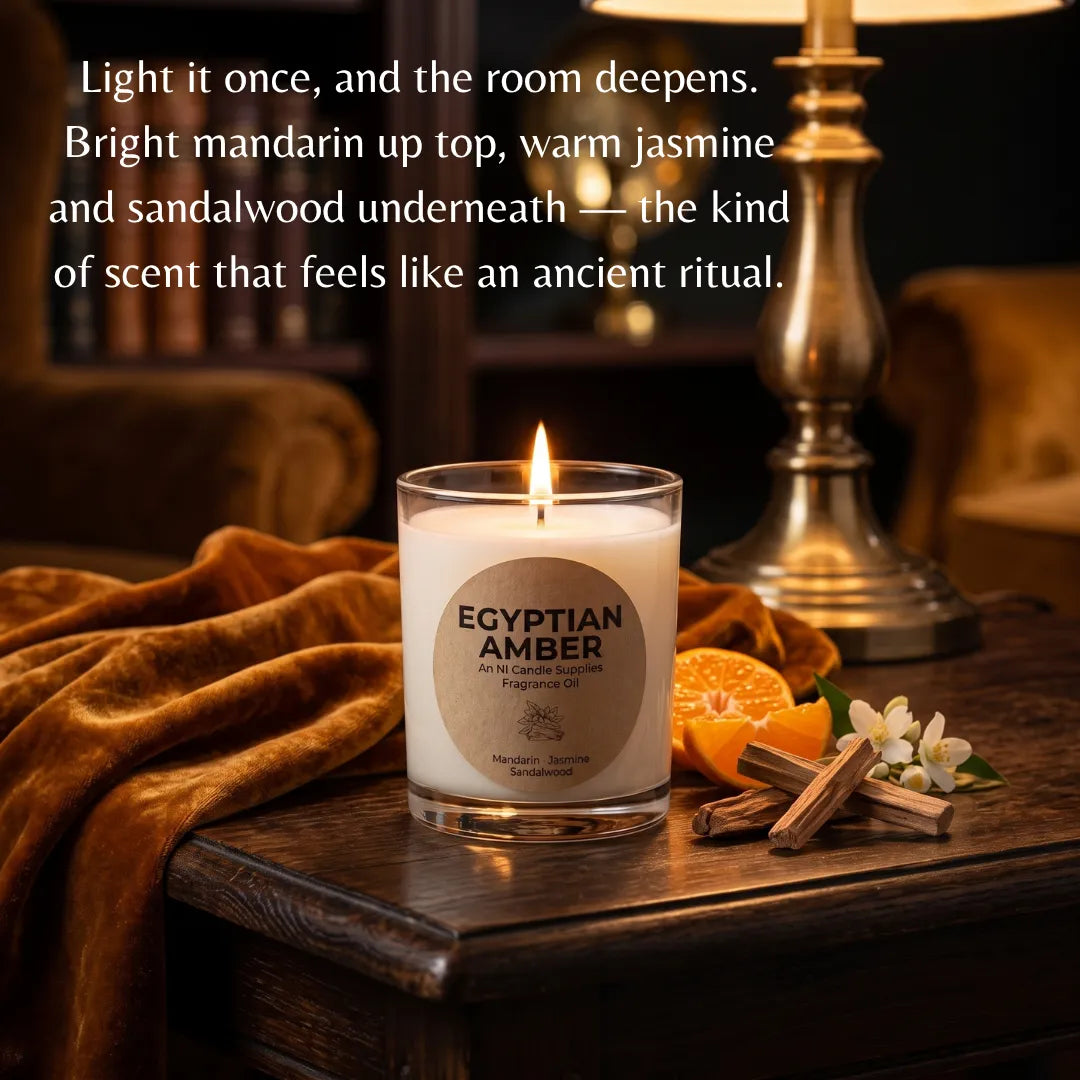A lit scented candle in a clear glass jar sits on a wooden table in a warmly lit room, with a brass lamp, orange slices, cinnamon sticks, and white flowers around it. White text at the top reads, 'Light it once, and the room deepens.