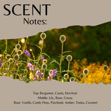 Scent Notes graphic featuring a floral field photo with thistle-like heads and purple flowers, overlaid with beige text sections reading 'SCENT Notes:' and a list of fragrance notes including Bergamot, Lily, Rose, Cocoa, Vanilla, Candy Floss, Patchouli, Amber, Tonka, and Caramel.