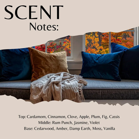Scent Notes graphic featuring a cozy living room scene with blue and brown pillows, a cream throw blanket, and autumn trees visible through the windows. Text at the top reads 'SCENT Notes:' and the bottom lists fragrance notes including cardamom, cinnamon, clove, apple, plum, fig, cassis, rum punch, jasmine, violet, cedarwood, amber, damp earth, moss, and vanilla.