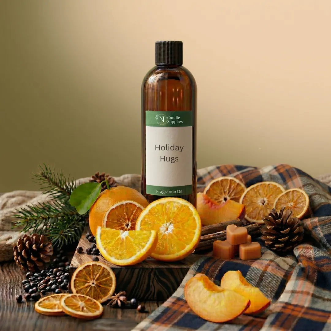 An amber glass bottle labeled 'Holiday Hugs' fragrance oil stands on a plaid fabric surface with orange slices, pinecones, dried orange slices, cinnamon sticks, and a few cubes around it. No person or animal is present, but this is a styled product scene rather than a plain studio cutout, so Product/Packaging fits better than Lifestyle.
