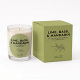 A glass jar candle with a white wax fill and a green circular label, shown next to its matching olive green square box. The label and box read 'LIME, BASIL & MANDARIN' and indicate fragrance oil by An Ni Candle Supplies.