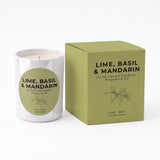 A white glass candle jar with a green circular label next to its matching olive green box, both labeled 'LIME, BASIL & MANDARIN' fragrance oil by An NI Candle Supplies.