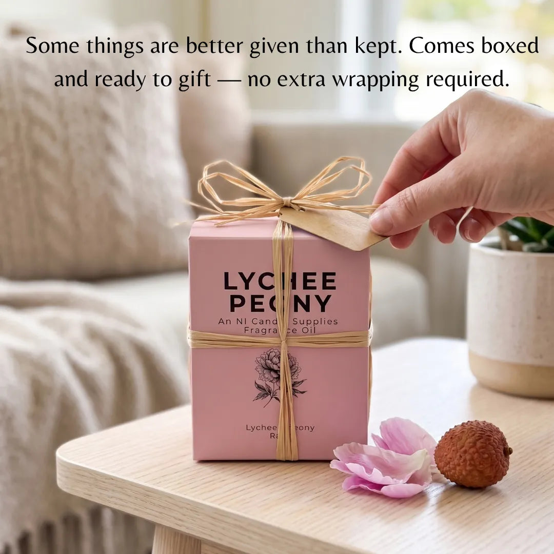 A pink Lychee Penny gift box tied with a natural jute ribbon and kraft paper tag, shown on a light wood table in a softly blurred indoor setting. A hand is touching the ribbon tag, and the text at the top reads, 'Some things are better given than kept.