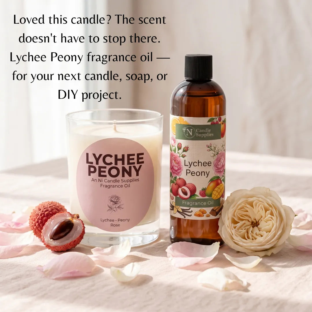 A bottle of Wn Candle Supplies Lychee Peony fragrance oil stands next to a glass jar candle with a matching pink label, styled on a light fabric surface with lychee fruit halves, a cream rose, and scattered petals. Text at the top reads, 'Loved this candle? The scent doesn't have to have to stop there.