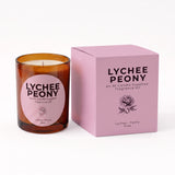 An amber glass jar candle with a pink circular label next to its matching pink packaging box, both labeled 'LYCHEE PEONY' by An Ni Candle Supplies, on a clean white background.