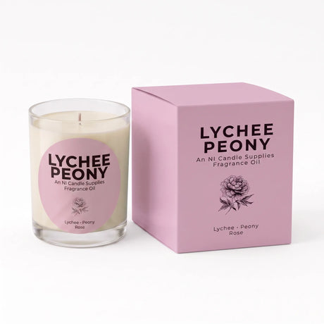 A Lychee Peony fragrance oil candle in a clear glass jar with cream-colored wax and a pink circular label, shown next to its matching pink square box on a white background.