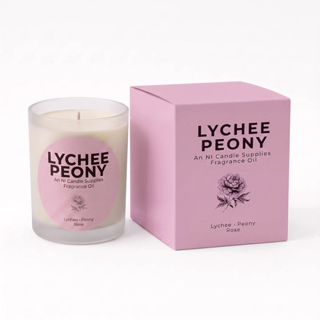 A Lychee Peony scented fragrance oil candle in a frosted glass jar next to its pink packaging box, featuring a pink circular label on the candle and black text on the box.