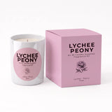 A white glass candle jar with a pink circular label next to its matching pink box, both printed with the text 'LYCHEE PEONY' and a rose illustration, on a clean white background.