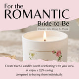 A lit white candle with floral illustrations on the label, set against a soft pink promotional graphic with text reading 'For the ROMANTIC Bride-to-Be' and 'Floral · Lily, Rose & Musk.'.