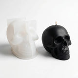 Black skull-shaped candle next to a white skull-shaped candle on a light gray background