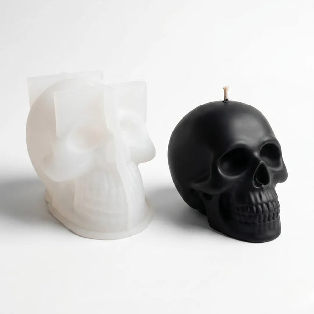 Black skull-shaped candle next to a white skull-shaped candle on a light gray background