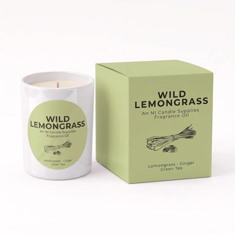 A white candle jar labeled 'WILD LEMONGRASS' next to its light green box, with the scent notes 'Lemongrass + Ginger' and 'Green Tea' visible on both the label and packaging.